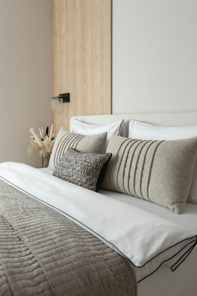 Bed layered with white bedding and grey and cream cushions